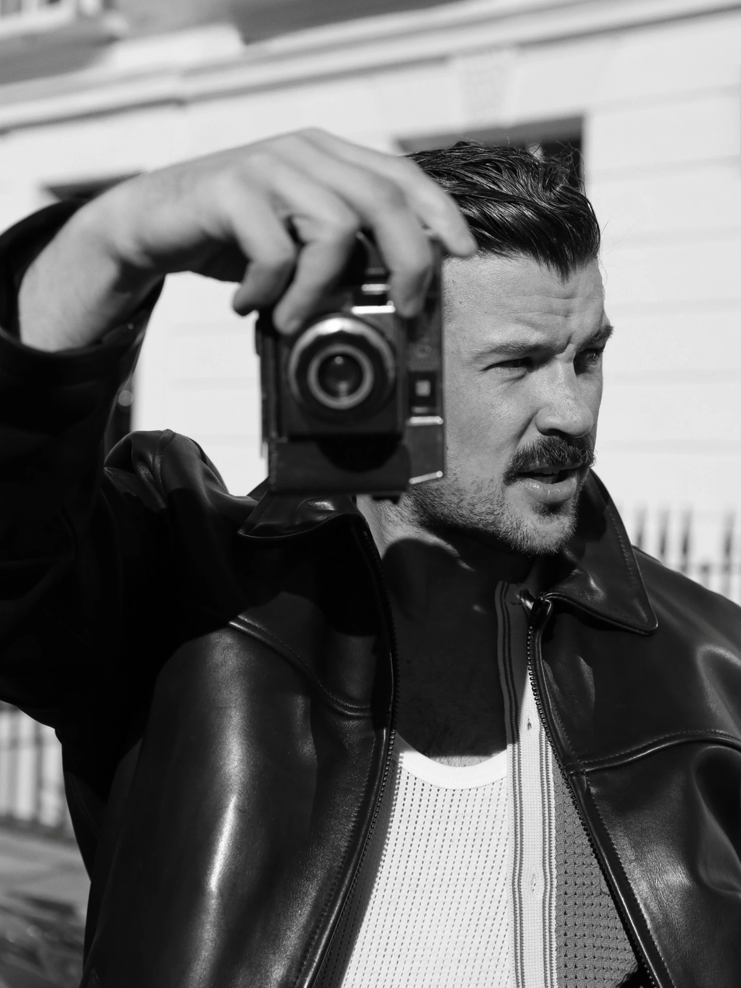Black-and-white portrait of a man raising a camera on a London street.