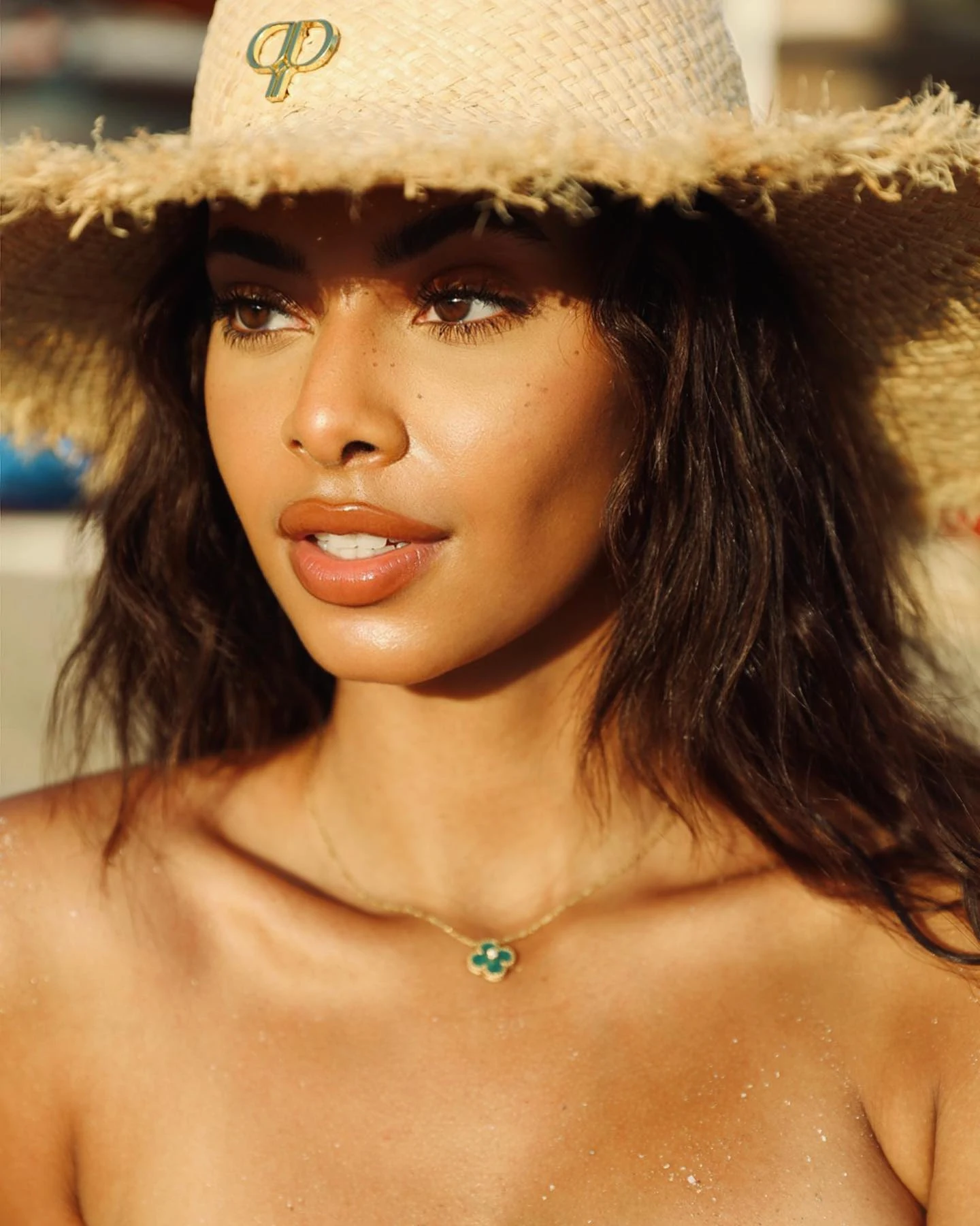 Sunlit portrait of a woman wearing a woven hat and a green pendant.